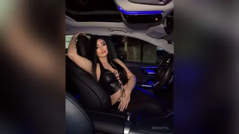Glamorous woman in a black lace corset sitting in a luxury car with moody blue ambient lighting.