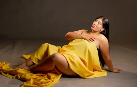 Elegant woman draped in a flowing yellow fabric sitting against a dark studio background with a serene mood.