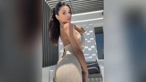 Elegant woman in a beige backless knit dress posing on a sunny modern balcony.