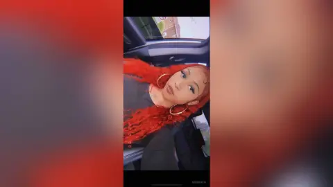 Young woman with vibrant red curly hair and gold hoop earrings relaxing in a car seat.