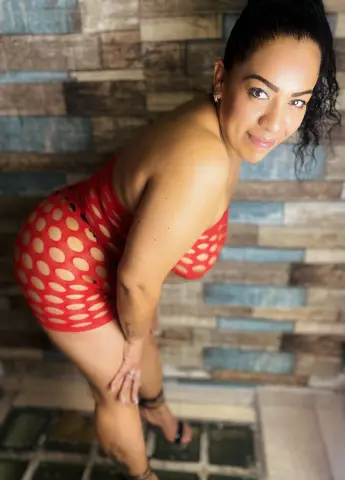 Smiling woman in a red polka dot bodysuit posing against a rustic textured stone wall.