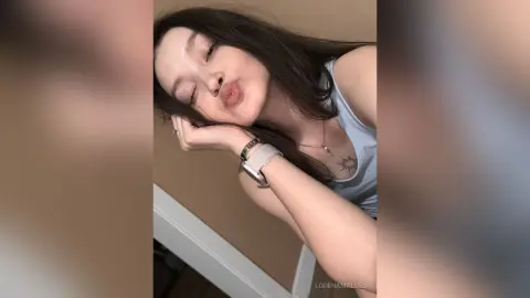 Young woman with long dark hair in a light blue tank top making a playful pouty face indoors.
