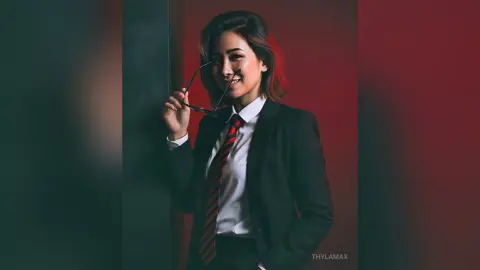 Smiling woman in a professional black suit and red striped tie posing confidently against a moody red background.