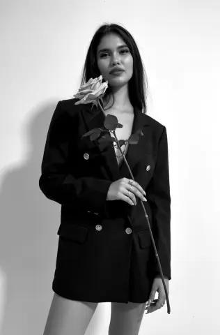 Elegant woman in a black blazer holding a single long-stemmed rose against a white background in black and white.