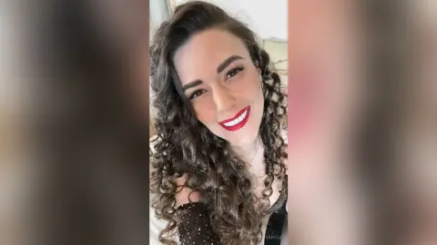MontseFerrera smiles with red lipstick and long curly brown hair while wearing a black lace top.