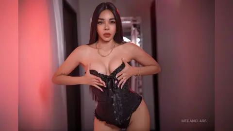Beautiful woman in black lace corset bodysuit posing in a moody, dimly lit room.