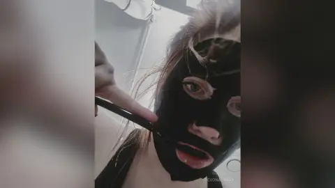 Young woman applying a black charcoal face mask in a bright bathroom for a relaxing skincare routine.