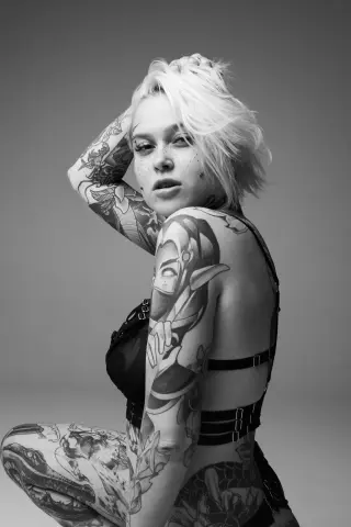 Tattooed woman in black lingerie posing for a moody black and white studio portrait.