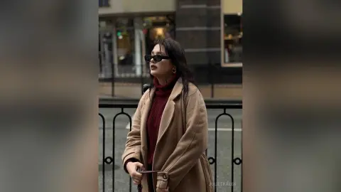 Stylish woman in a tan wool coat and burgundy turtleneck wearing sunglasses on a city street.