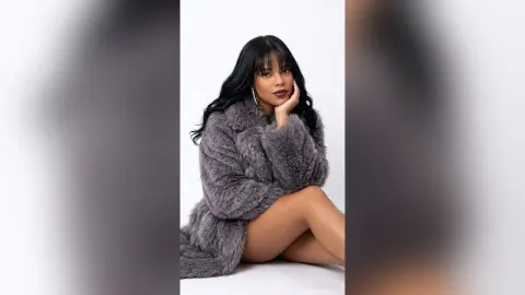 Elegant woman in a grey faux fur coat posing against a white background with a sophisticated mood.