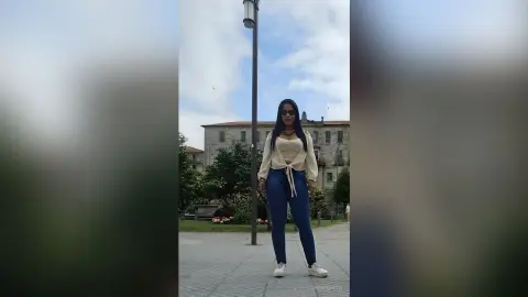 Stylish woman in a cream tie-front top and blue jeans standing outdoors near a historic stone building.