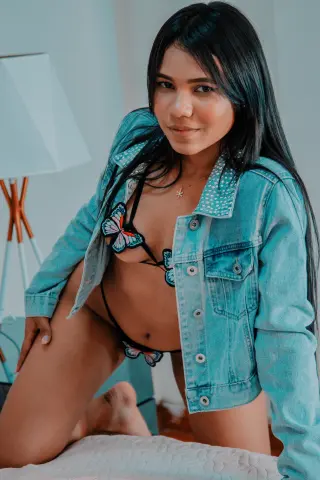 Smiling woman in a denim jacket and butterfly bikini relaxing in a bright indoor setting.
