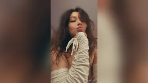 RitaMoonllight pouts her lips while wearing a white, ruched, long-sleeve top that leaves her shoulders bare.