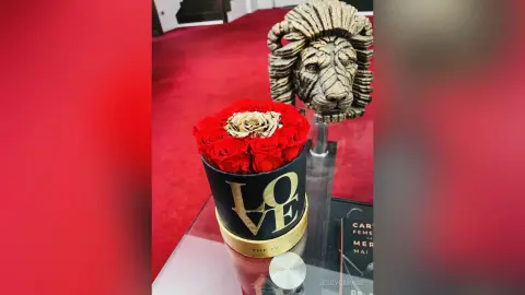 JessycaPage displays a black hat box filled with red and gold roses next to a gold lion head statue on a glass surface.