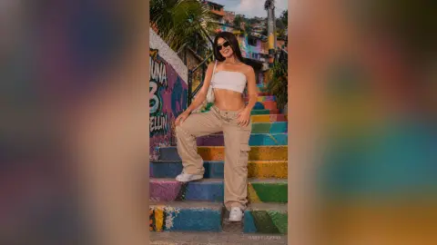 Smiling woman in white crop top and beige cargo pants posing on colorful urban street stairs.