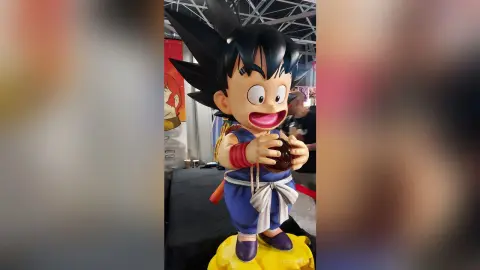 Goku figure statue in blue and white outfit standing on a yellow base at an anime convention exhibit.