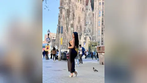 Stylish woman in a black evening dress posing in front of the Sagrada Familia in Barcelona.