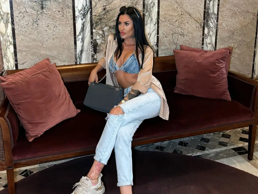 Stylish woman in denim crop top and light jeans sitting on a velvet sofa in a luxury marble interior.