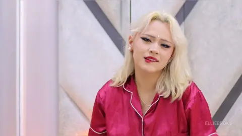Blonde woman in red satin pajamas smiling in a modern, bright interior setting.