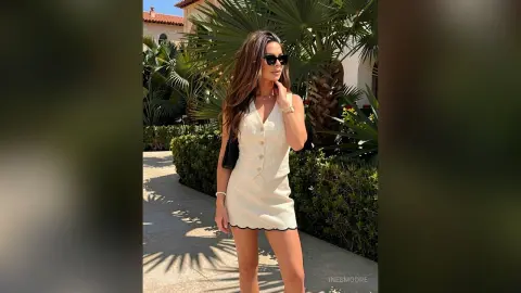 Stylish woman in a white linen vest and mini skirt outfit walking through a sunny tropical garden.