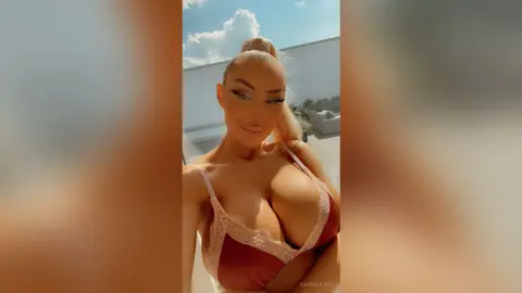 VeneraSecret poses outdoors in a brown lace bra, showing off her large breasts and blonde hair tied in a high ponytail.