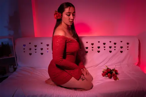 Young woman in a red lace dress sitting on a bed in moody red lighting with a bouquet of roses.