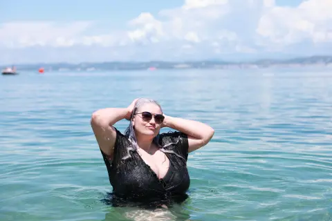 Curvy woman in a black swimsuit and sunglasses relaxing in clear turquoise ocean water on a sunny day.