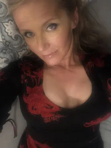 Blonde woman in a black and red floral print dress relaxing on a patterned pillow in a cozy mood.