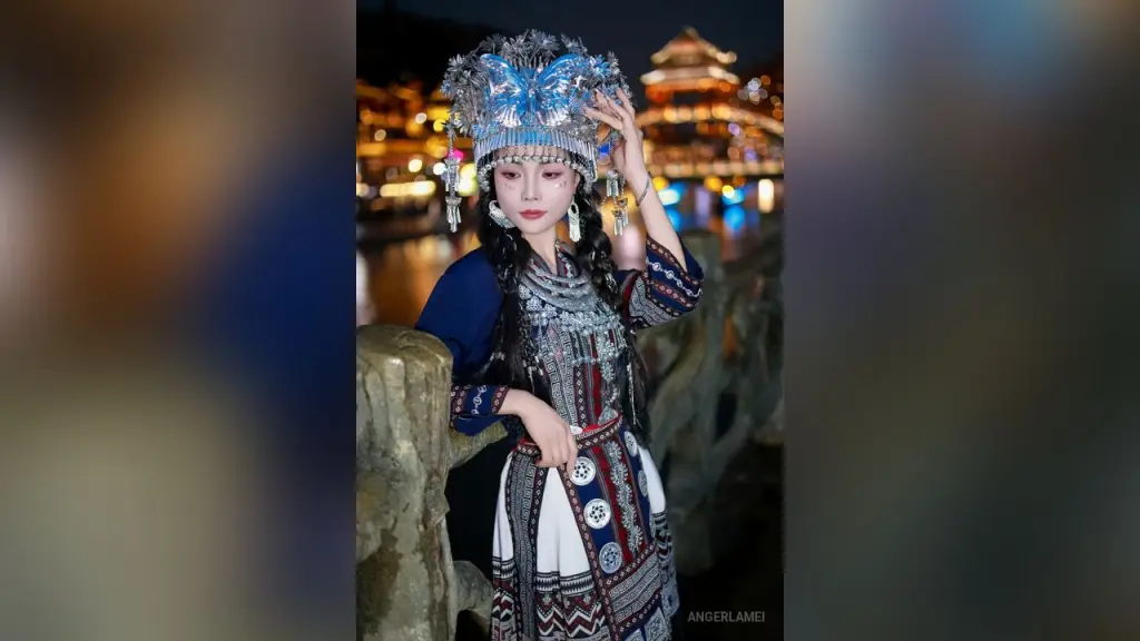 AngerlaMei — AngerlaMei wears an elaborate silver headpiece and traditional blue and red patterned ethnic clothing while standing outdoors at night.