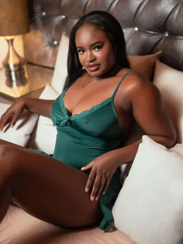 Beautiful Black woman in a green satin chemise relaxing on a bed in a cozy, moody bedroom setting.