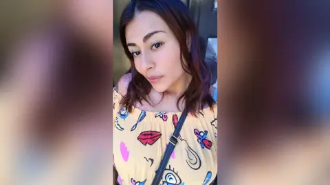 Young woman in a yellow floral print top posing for a casual outdoor selfie with a relaxed mood.