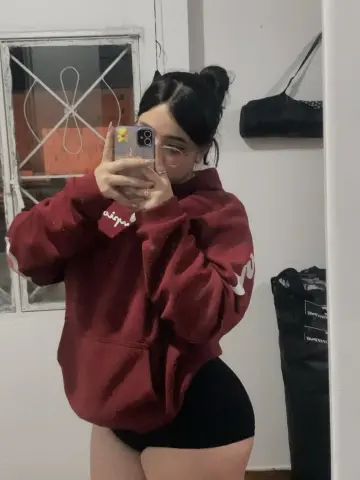 Young woman in a cozy burgundy oversized hoodie and black shorts taking a casual mirror selfie indoors.