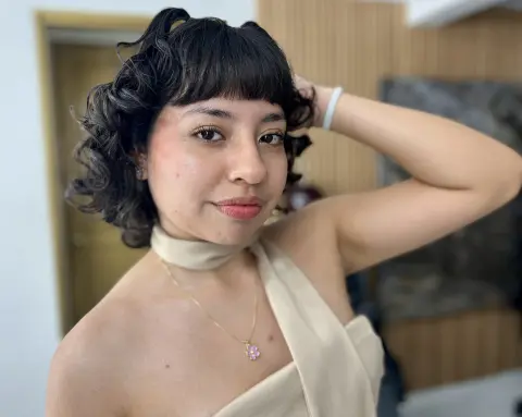 Smiling woman in a cream halter top and gold necklace posing in a bright indoor setting.