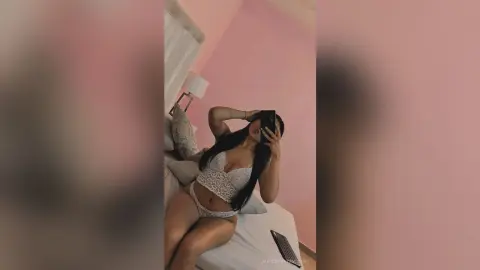 Young woman in white lace lingerie relaxing on a bed in a cozy pink bedroom.
