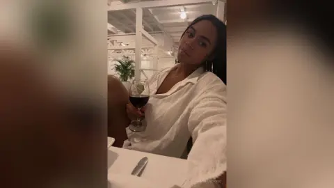 Young woman in a white linen shirt relaxing with a glass of red wine in a modern, brightly lit restaurant.