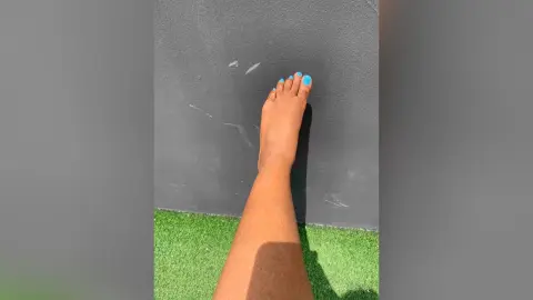 Close-up of a person's bare foot with bright blue nail polish resting against a dark grey textured wall.