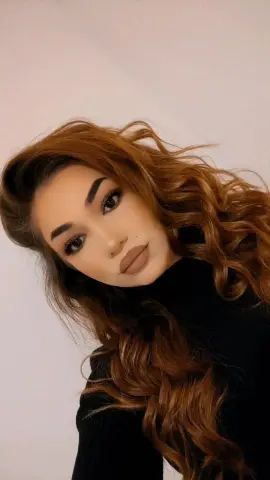 Beautiful woman with wavy brown hair wearing a black turtleneck sweater against a plain white background.