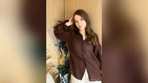 PaisleyMoore — PaisleyMoore leans against a wall in a brown button-down shirt and white pants.