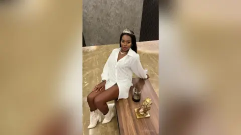 Elegant woman in a white button-down shirt and white boots sitting gracefully in a modern luxury interior.