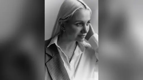 Moody black and white portrait of a blonde woman in a white shirt and pinstripe blazer looking away.