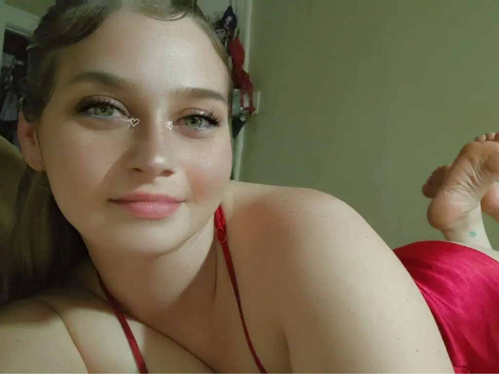 Smiling young woman in a red satin top relaxing indoors with a soft, natural glow.