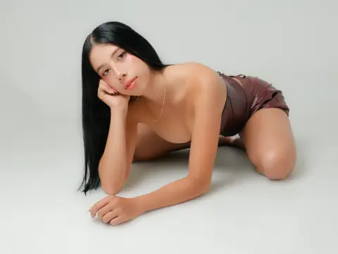 Young woman with long black hair in brown shorts posing gracefully against a neutral studio background.