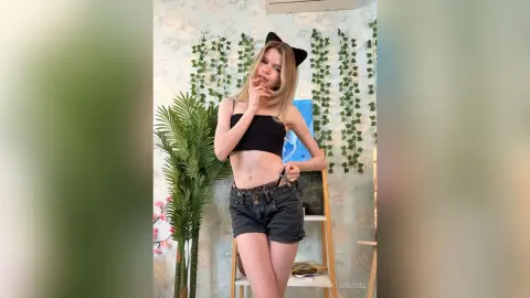 UnataMigdel poses in a black crop top and short denim shorts with cat ears on her head.