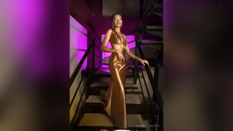 Elegant woman in a shimmering bronze satin gown posing on a modern staircase under moody purple lighting.