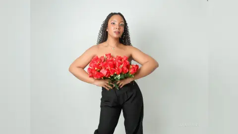 Young woman in black trousers holding a large bouquet of red roses against a white studio background.