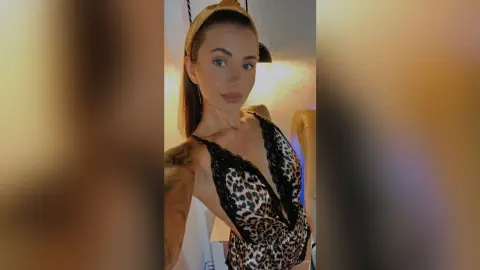 Young woman in a leopard print lace camisole posing in a brightly lit room.