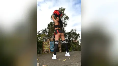 AmeliaStell stands outdoors in a black and red crop top and skirt set with black thigh-high socks and white sneakers.