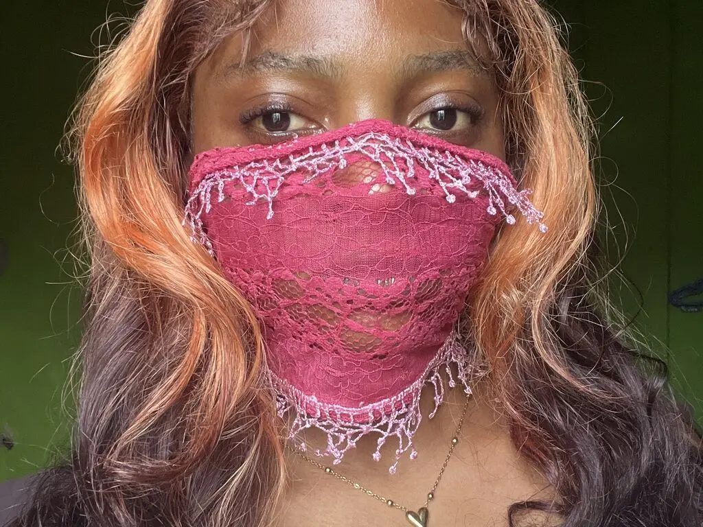 BiancaJasmine wears a pink lace mask covering her nose and mouth, showing her eyes and long, wavy reddish-brown hair.