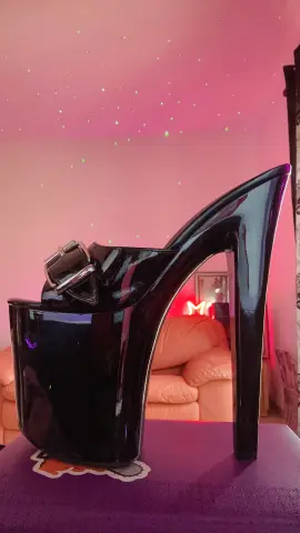 Shiny black patent leather platform high heel sandals with a large buckle on a purple surface.