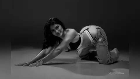 Young woman in Calvin Klein underwear and denim jeans posing on a studio floor in a moody black and white portrait.